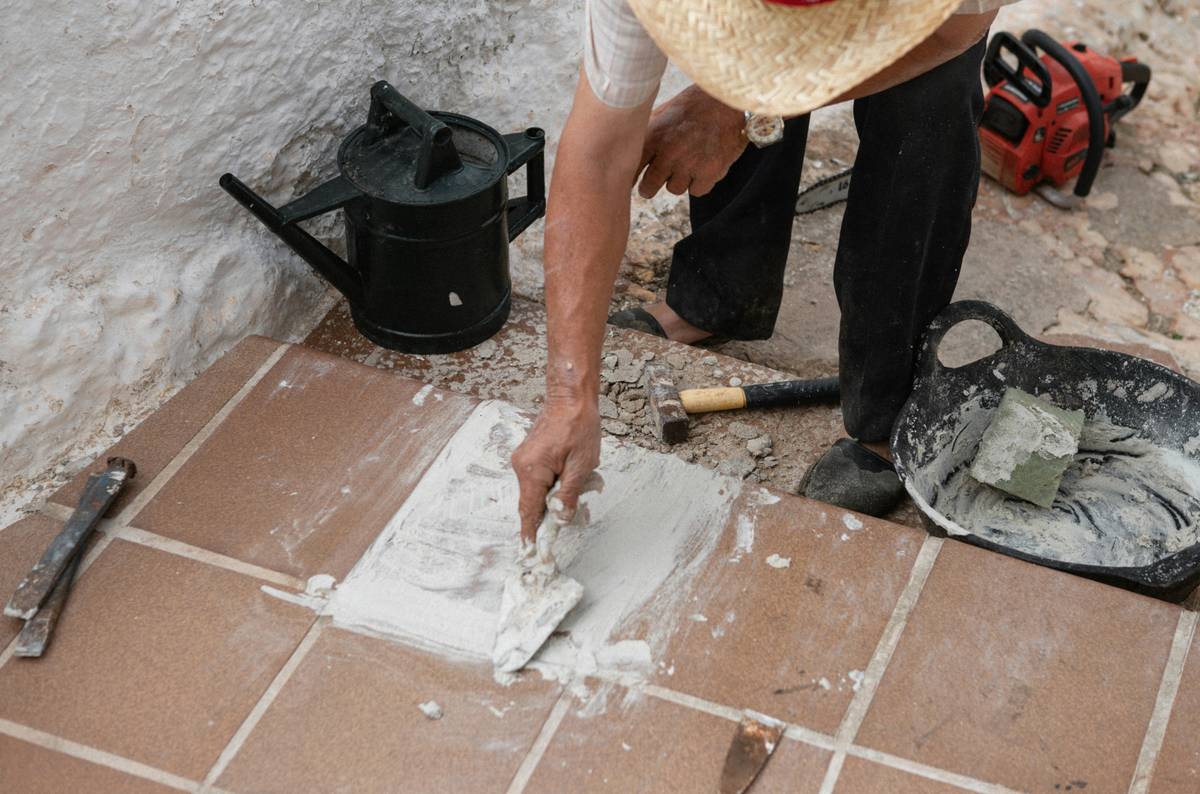 Hand holding a project source caulk gun while applying silicone sealant along a bathtub edge